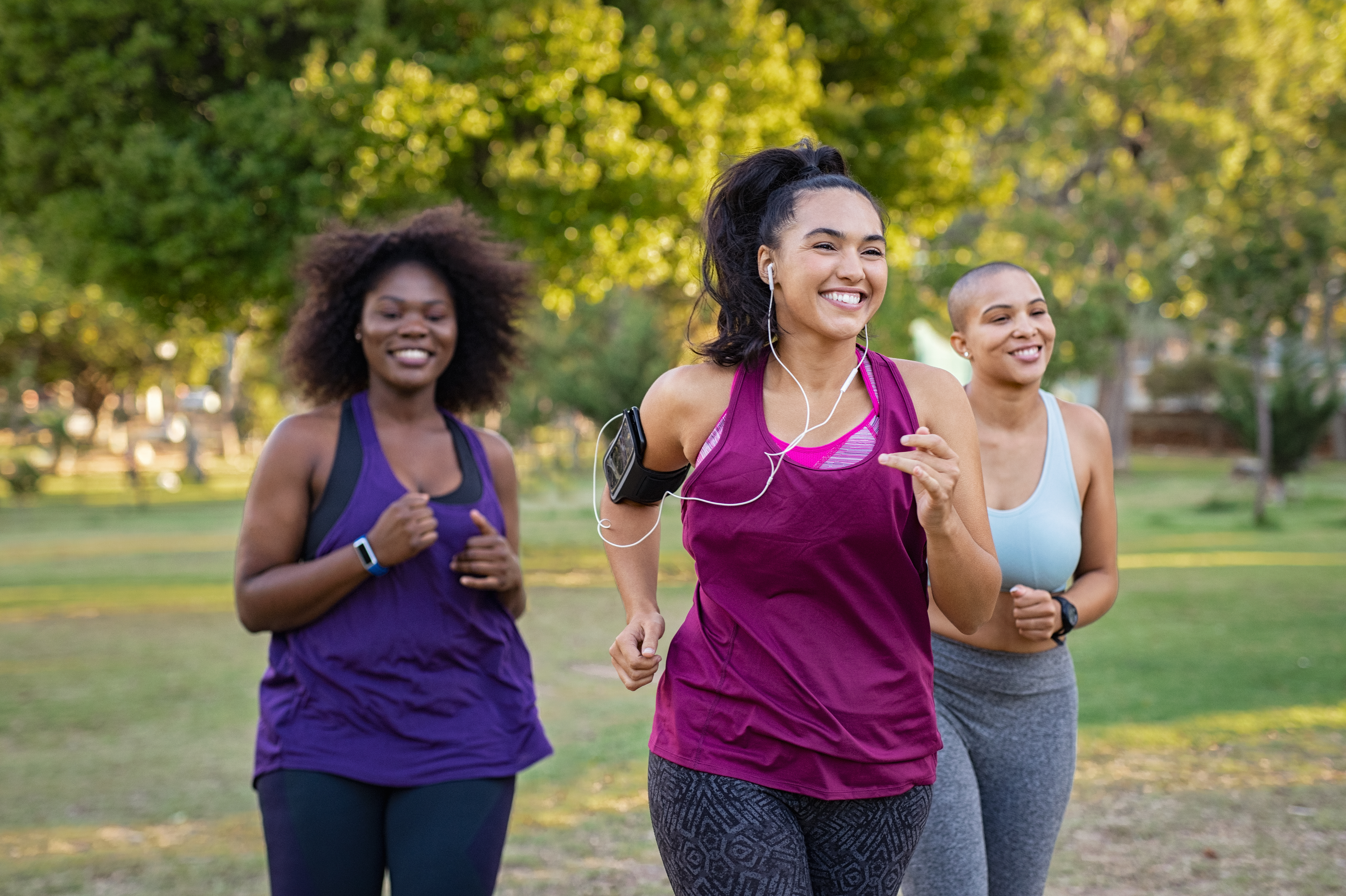three women smiling while jogging in a park
